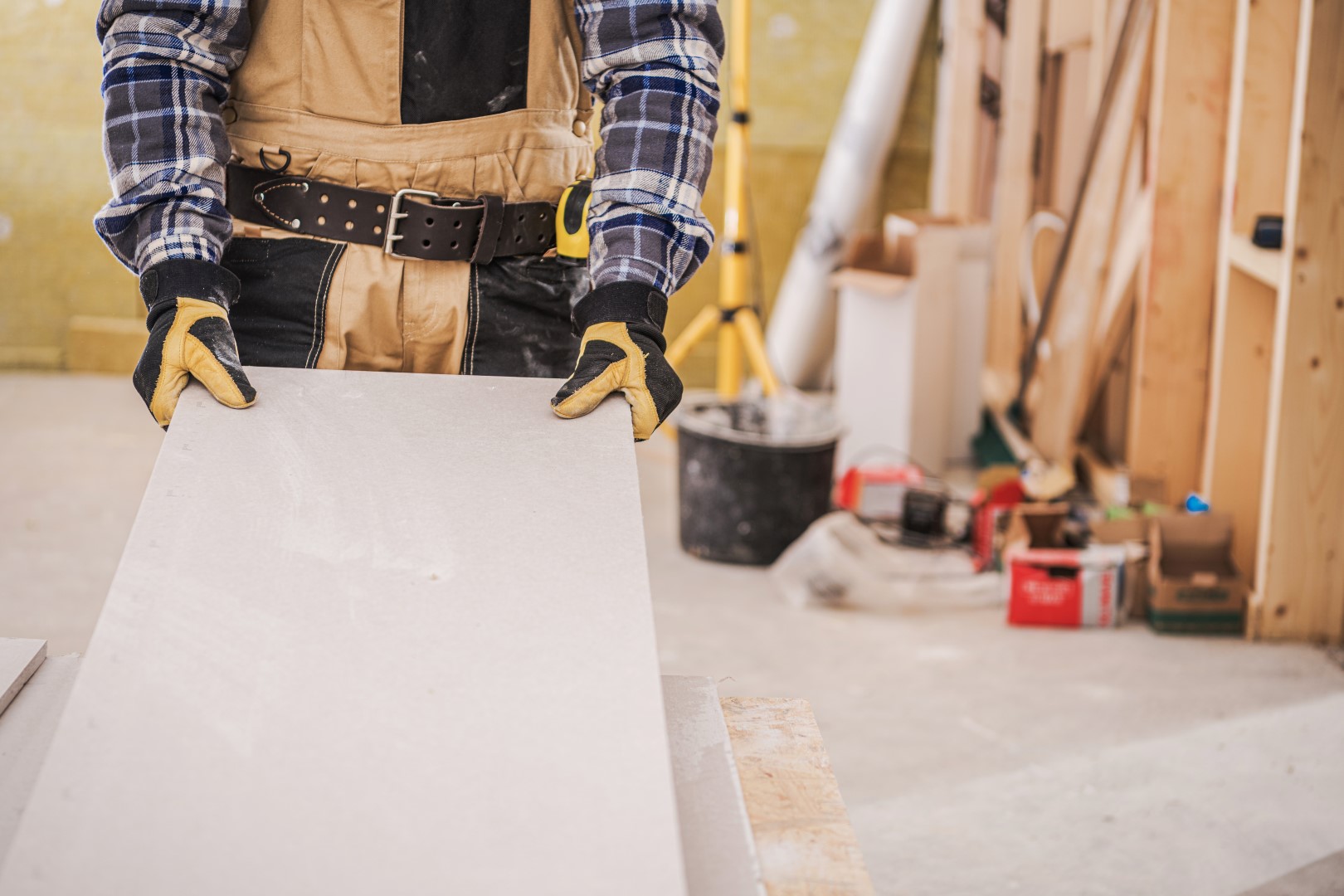 Male Construction Worker Holding Long Piece Of Gray Drywall Material Ready To Be Installed On House Wall.