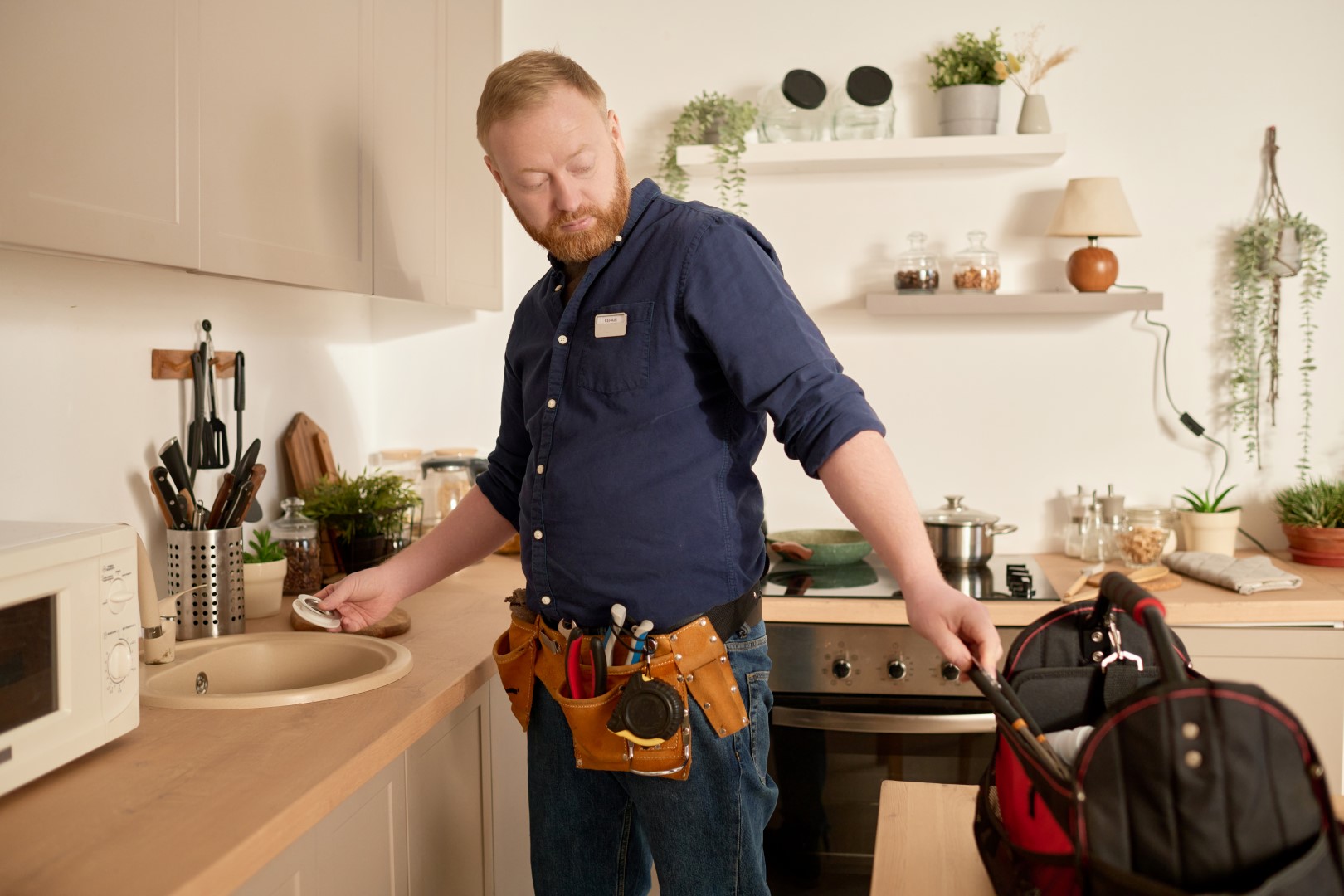 Worker using his tools from the bag to repair sink in the kitchen at home